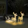Christmas reindeer and sleigh decorations illuminated in a snowy garden at night, with a house and tree in the background. Podgląd zdjęcia produktu