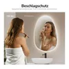 A woman applying makeup in front of a lighted mirror in a bathroom. Náhľad obrázku produktu