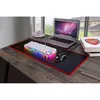 A gaming keyboard and mouse setup on a wooden desk, with a laptop and books in the background. Produktbild-Vorschau