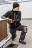 A man is kneeling on a floor, wearing work clothes and holding a tool. Anteprima dell’immagine prodotto