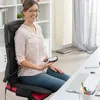 A woman is sitting in a chair with a massage mat, holding a remote control. Náhľad obrázku produktu