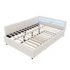 A white upholstered bed frame with a slatted mattress support and LED lighting in the headboard is shown against a white background. Podgląd zdjęcia produktu