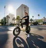 A man is riding an electric bike on a sunny day in a city with palm trees and modern buildings. Produktbild-Vorschau