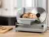 A bread slicer with a loaf of bread on it sits on a wooden table, with sliced bread on a cutting board next to it. Náhľad obrázku produktu