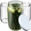 Three glass jars, one filled with pickles, and a white lid are arranged on a white background. Podgląd zdjęcia produktu
