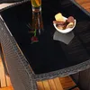 A close-up view of a black glass tabletop on a rattan table, with a drink and a bowl of snacks. Anteprima dell’immagine prodotto