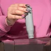 A person's hand with glittery nails is holding a gray water filter cartridge over a clear plastic container. Náhled obrázku produktu