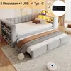 A light gray upholstered daybed with a pull-out trundle bed, set up in a room with a rug and a small robot vacuum cleaner. The daybed has built-in shelving and LED lighting. Produktbild-Vorschau