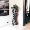 A modern metal wine rack filled with wine bottles and topped with a potted plant, placed in a room next to a framed picture and a doorway. Podgląd zdjęcia produktu