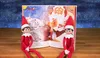 Two Elf on the Shelf dolls are sitting in front of an open pop-up book featuring Santa Claus. Produktbild-Vorschau