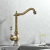 A vintage-style kitchen faucet is shown in a close-up shot against a textured metallic background. A glass of water with lemon slices is visible to the right. Náhľad obrázku produktu