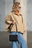 A woman stands in front of a concrete wall, holding a black bag. Produktbild-Vorschau