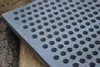 A close-up of a perforated metal grate, likely a stove or oven grate, resting on a wooden surface. Produktbild-Vorschau