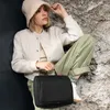 A woman is sitting on rocks, holding a black toiletry bag. Anteprima dell’immagine prodotto