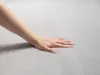 A hand touching a soft, light gray carpet. Produktbild-Vorschau