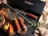 A set of knives is displayed on a cutting board with some ingredients and a gift box. Náhled obrázku produktu
