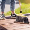 A person is sweeping a wooden deck with a broom. Podgląd zdjęcia produktu