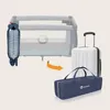 A baby crib is shown folded into a compact form next to a suitcase and a carrying bag, illustrating its portability. Produktbild-Vorschau