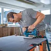 A man is using a blue and black jigsaw to cut a circular shape into a dark gray surface. Anteprima dell’immagine prodotto