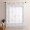 A transparent curtain with a brown embroidered pattern hangs on a window rod. A vase with lavender and a small white object are placed on a wooden surface to the left of the window. Produktbild-Vorschau