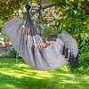 A person relaxing in a gray hammock chair hanging from a tree branch in a garden. Produktbild-Vorschau