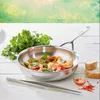 A stainless steel frying pan with cooked shrimp and vegetables, placed on a white wooden table with a bunch of cilantro, bread slices, and a small bowl of sauce. Voir les images du produit
