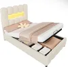 A beige upholstered bed with under-bed storage, a flower pillow, and patterned bedding is shown with the mattress lifted to reveal the storage compartments. Produktbild-Vorschau