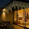 Outdoor patio area at night with icicle lights strung across the roofline, a table and chairs, and a view into a living room decorated for Christmas. Anteprima dell’immagine prodotto