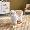 A white rocking sheep toy sits on a yellow and white checkered rug in a child's room. A white cabinet with cloud cutouts is visible in the background, along with a chair with a stuffed animal. Produktbild-Vorschau