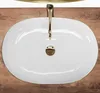 A top-down view of a white oval sink with a gold rim and faucet, set against a wooden background. Náhled obrázku produktu