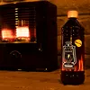 A kerosene heater and a bottle of kerosene fuel in an outdoor setting with a brick wall background. Produktbild-Vorschau