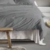 A close-up view of a bed with gray striped bedding and a white bed skirt. Produktbild-Vorschau