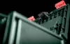 A close-up shot of a green plastic tool tracker with red and black components, against a black background. Voir les images du produit