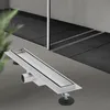 A linear shower drain is shown in the foreground, with a tiled shower area in the background. Náhled obrázku produktu