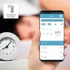 A hand holding a smartphone displaying a smart home heating control app, with a clock and a person sleeping in the background. Náhľad obrázku produktu
