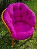 A bright pink cushion on a rattan chair placed on a grassy lawn. Produktbild-Vorschau
