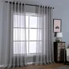 A window with light gray sheer curtains hanging in front of it, with a small wooden dresser and a lamp to the right. Produktbild-Vorschau