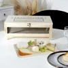 A wooden cheese cellar with a serving tray and various cheeses on a white table. Voir les images du produit