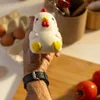A hand holding a chicken-shaped stress toy in a kitchen setting with eggs and tomatoes visible. Voir les images du produit