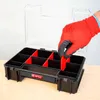 A hand wearing a red glove is placing a red divider into a black organizer box with multiple compartments. Náhled obrázku produktu