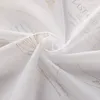 A close-up of white sheer fabric with gold printed text and patterns. Produktbild-Vorschau