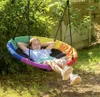 A young girl is relaxing in a rainbow-colored nest swing in a backyard setting. Produktbild-Vorschau