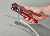 A hand is using a wire stripper tool to strip the insulation off a multi-conductor cable. Produktbild-Vorschau