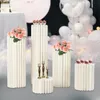A set of white cylindrical pedestals of varying heights, decorated with flowers and cupcakes, arranged for a party or wedding. Podgląd zdjęcia produktu