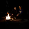 Two people are roasting marshmallows over a fire pit at night. Náhľad obrázku produktu
