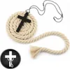 A black cross pendant on a necklace is placed on a coiled beige rope, with a separate piece of rope to the side. A circular logo with a white cross and snake is in the bottom left corner. Náhled obrázku produktu