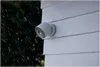A security camera mounted on the side of a house during a rain shower. Voir les images du produit
