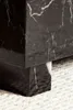 A close-up of the corner of a black marble-look coffee table with white veining, resting on a textured white rug. Voir les images du produit