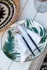 A place setting on a white wooden table with a tropical-themed plate, napkin, and cutlery. Voir les images du produit