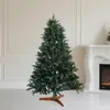 A green artificial Christmas tree with a wooden stand is shown in a room with a fireplace and ornate wall molding. Produktbild-Vorschau
